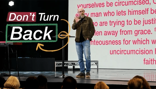 A bearded man in a green jacket preaches on stage in front of a screen with scripture. Text overlay says 'Don't Turn Back'.